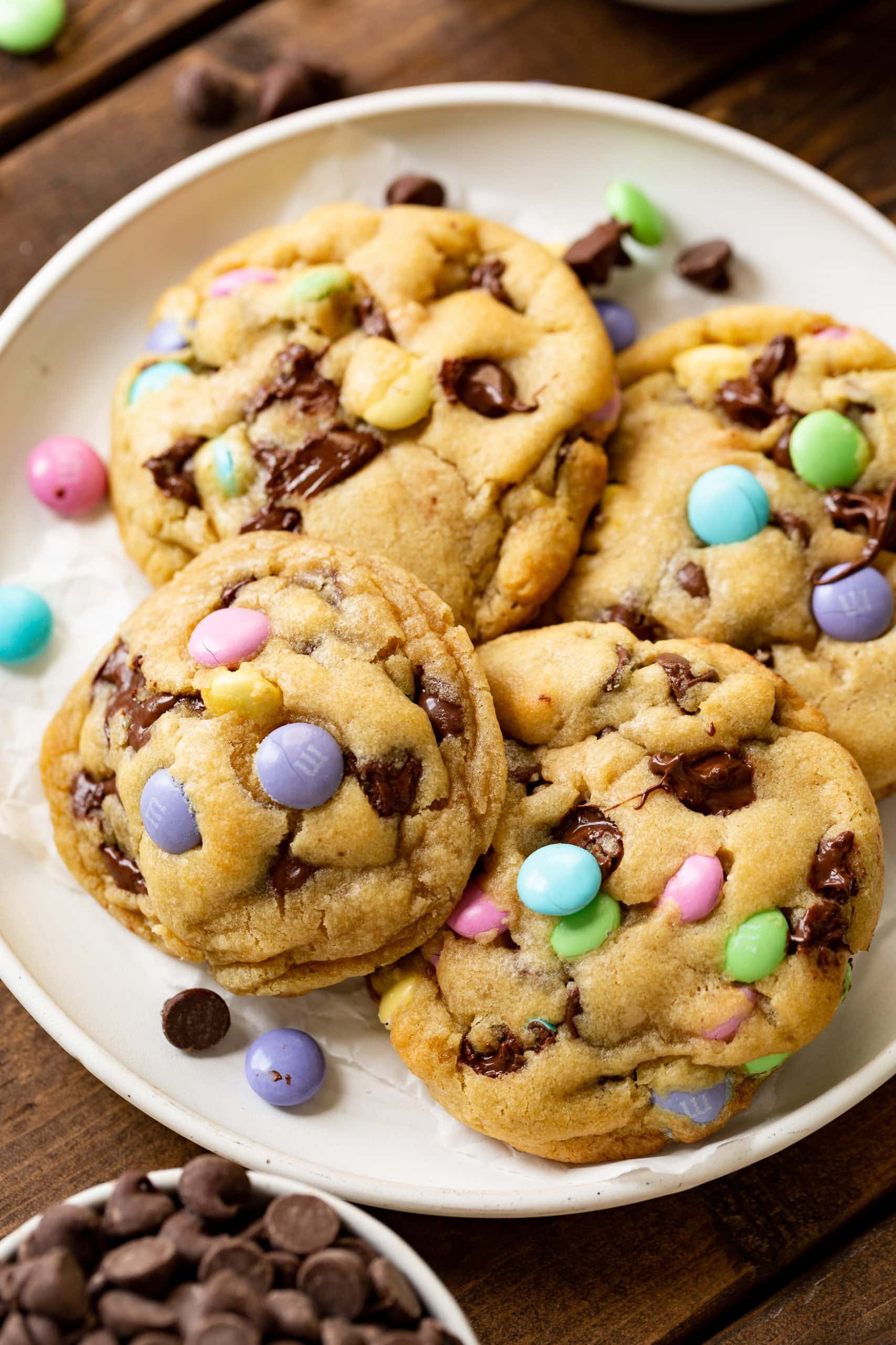 a photo of a white serving plate full of thick and golden Easter m&m chocolate chip cookies. a photo of a white serving plate full of thick and golden Easter m&m chocolate chip cookies.