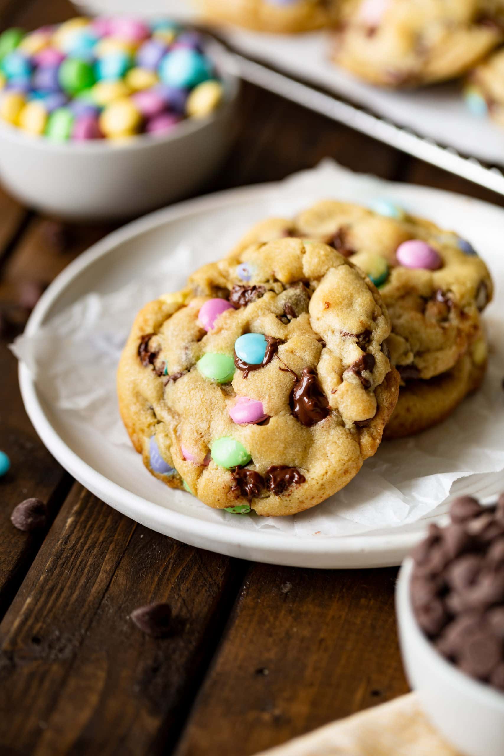 a photo of three large chocolate chip cookies loaded with Easter m&m's sitting on a small white saucer. a photo of three large chocolate chip cookies loaded with Easter m&m's sitting on a small white saucer.