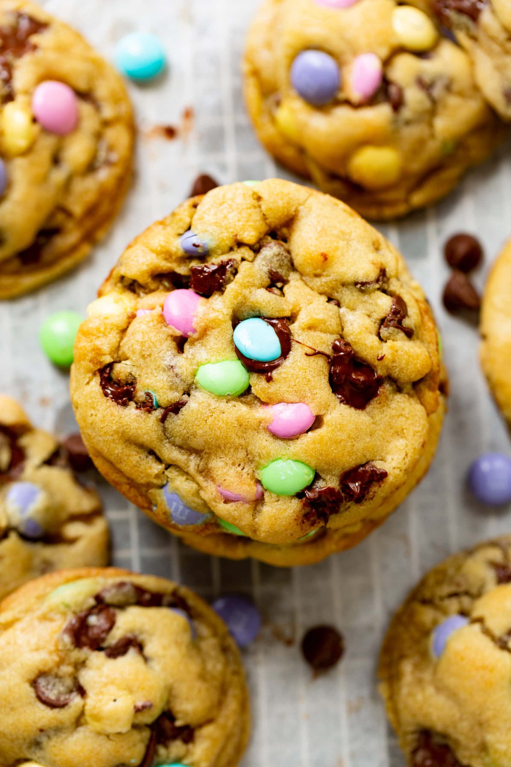 a photo of a single golden loaded chocolate chip Easter m&m cookie stacked on top of another cookie surrounded by other cookies. a photo of a single golden loaded chocolate chip Easter m&m cookie stacked on top of another cookie surrounded by other cookies.