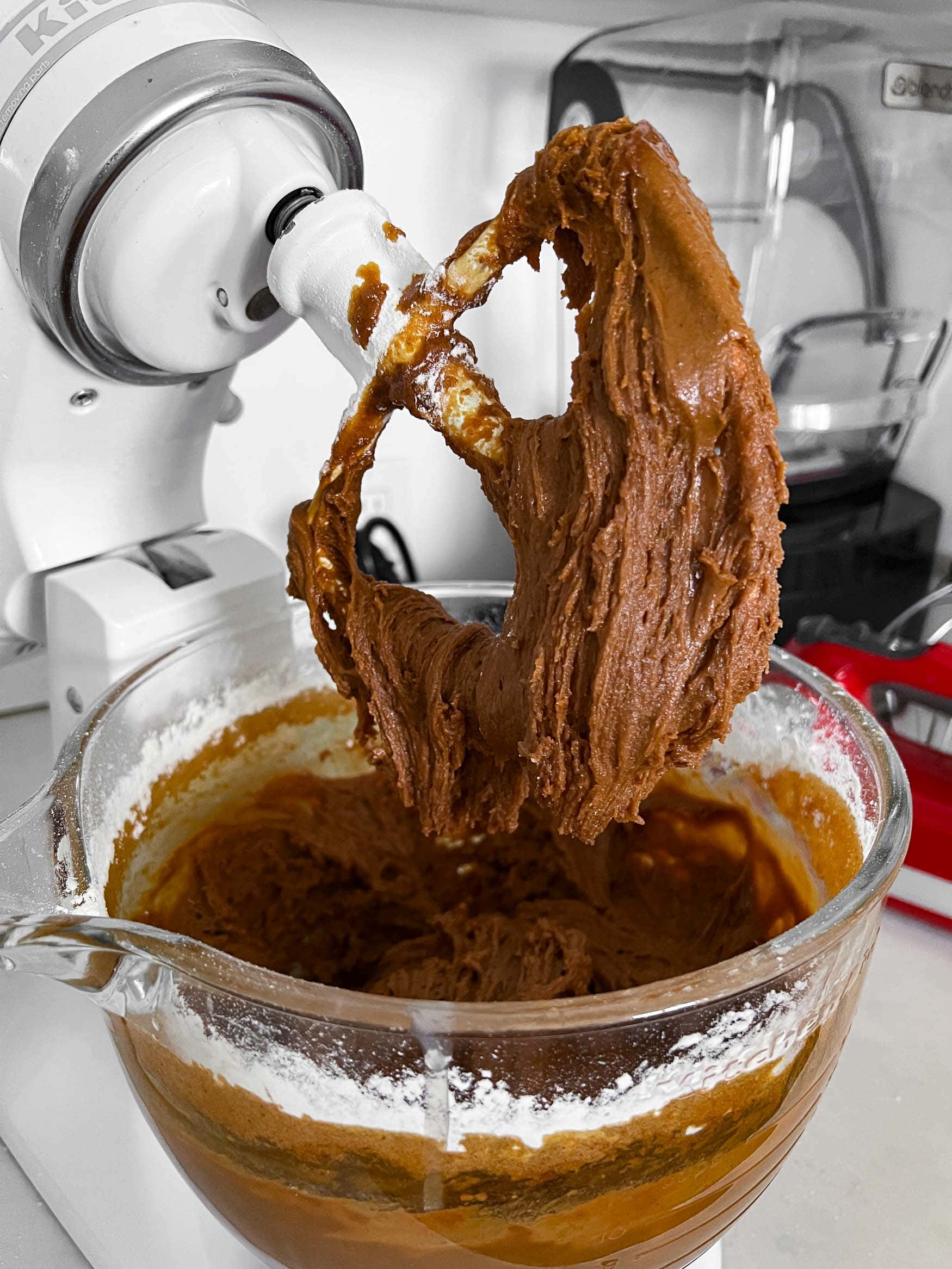 a photo of the glass bowl of a stand mixer full of gingerbread men cookie dough. the mixing paddle has been lifted so you can see the consistency of the dough falling off the paddle. a photo of the glass bowl of a stand mixer full of gingerbread men cookie dough. the mixing paddle has been lifted so you can see the consistency of the dough falling off the paddle.