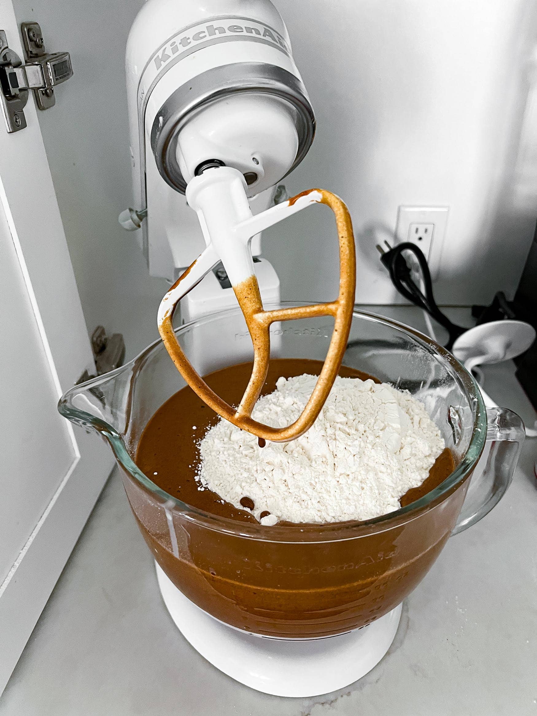 a photo of gingerbread cookie batter in the glass mixing bowl of a stand mixer with a cup of flour sitting on top ready to mix in. a photo of gingerbread cookie batter in the glass mixing bowl of a stand mixer with a cup of flour sitting on top ready to mix in.