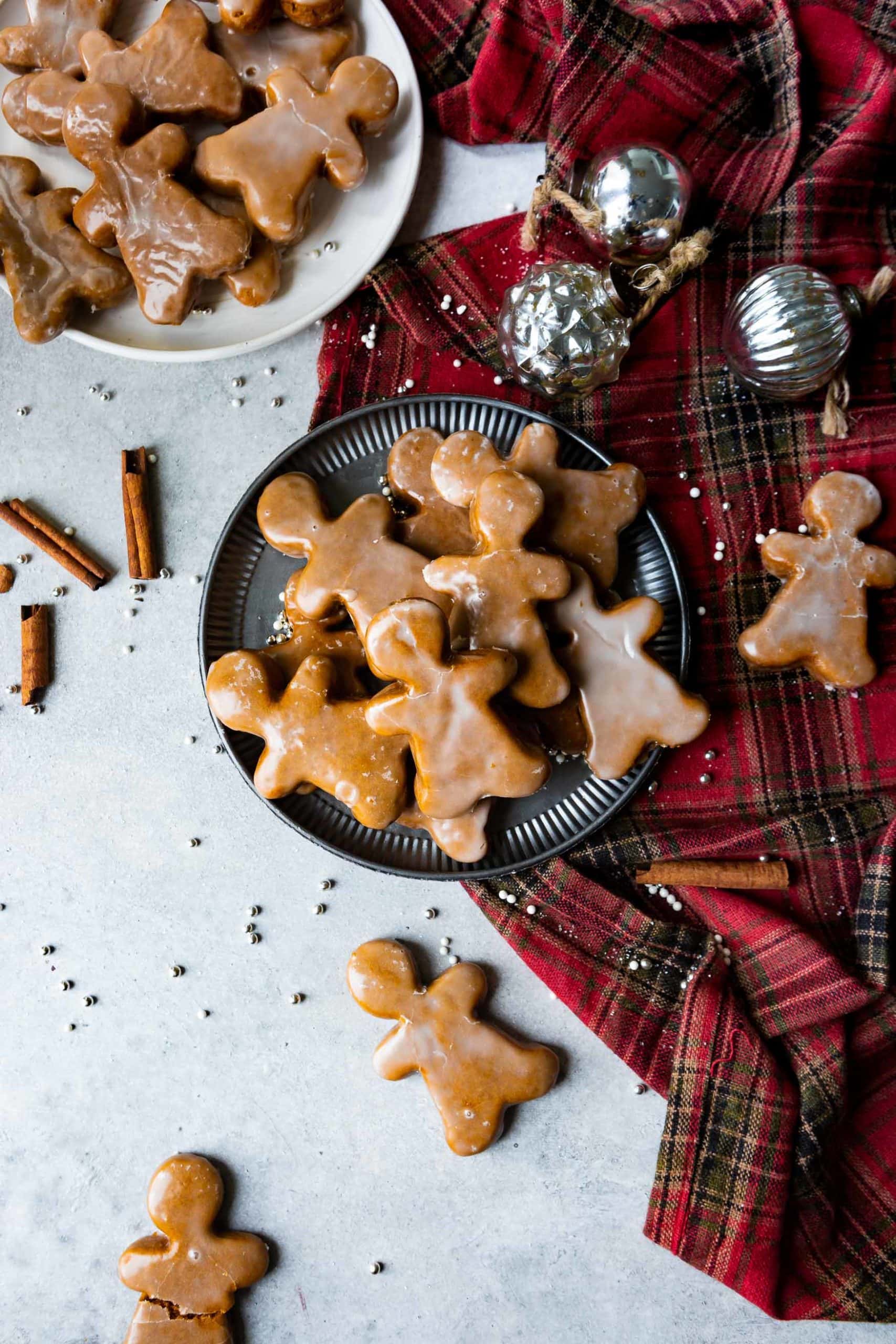 a photo of a plate piled high with thick and chewy gingerbread men cookies. the plate is sitting on a ruffled red plaid tablecloth and small silver decorative balls are scattered around it. a photo of a plate piled high with thick and chewy gingerbread men cookies. the plate is sitting on a ruffled red plaid tablecloth and small silver decorative balls are scattered around it.