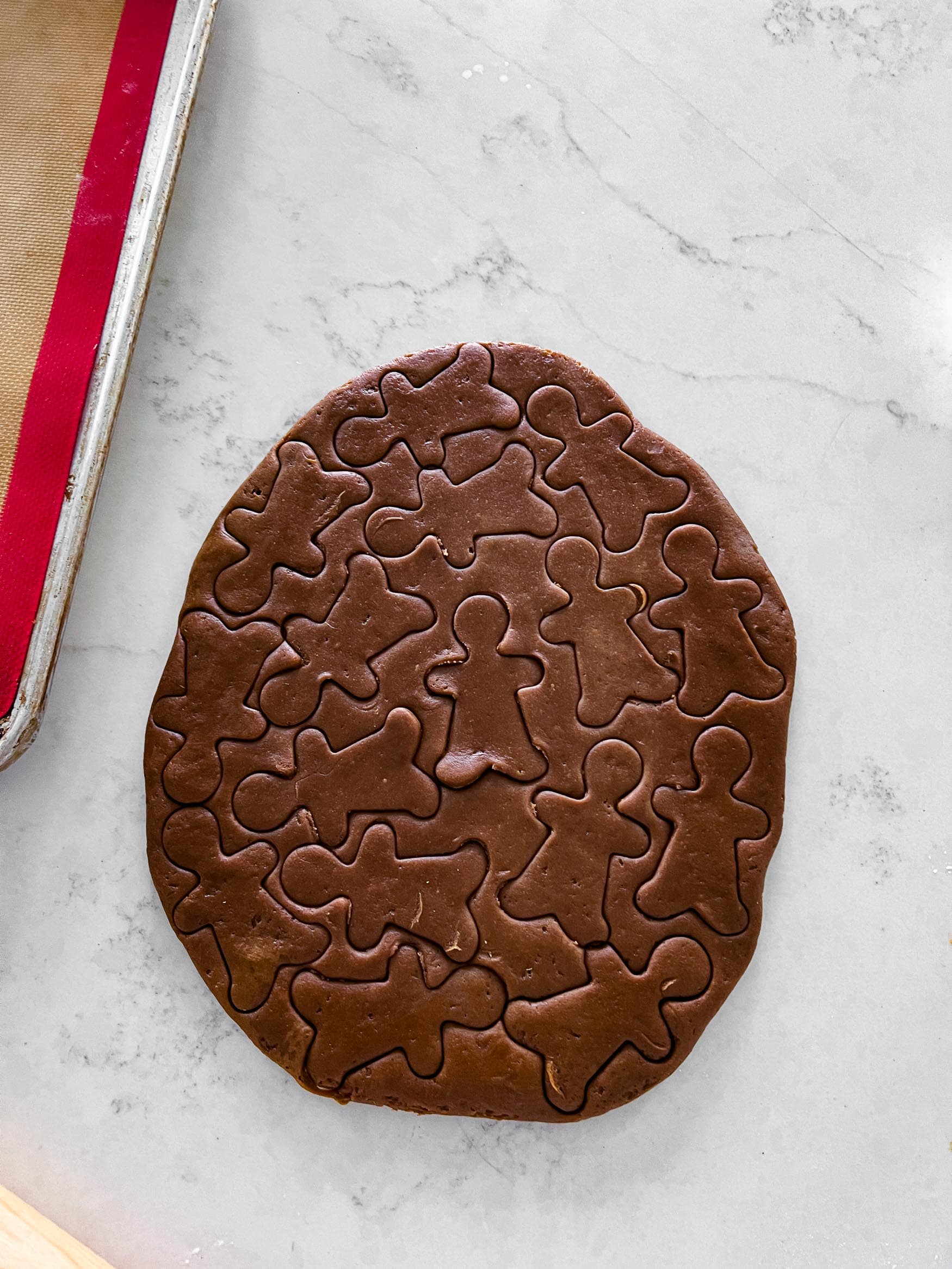 a photo of gingerbread cookie dough rolled out on the counter top with little gingerbread men cut into the dough all over. a photo of gingerbread cookie dough rolled out on the counter top with little gingerbread men cut into the dough all over.