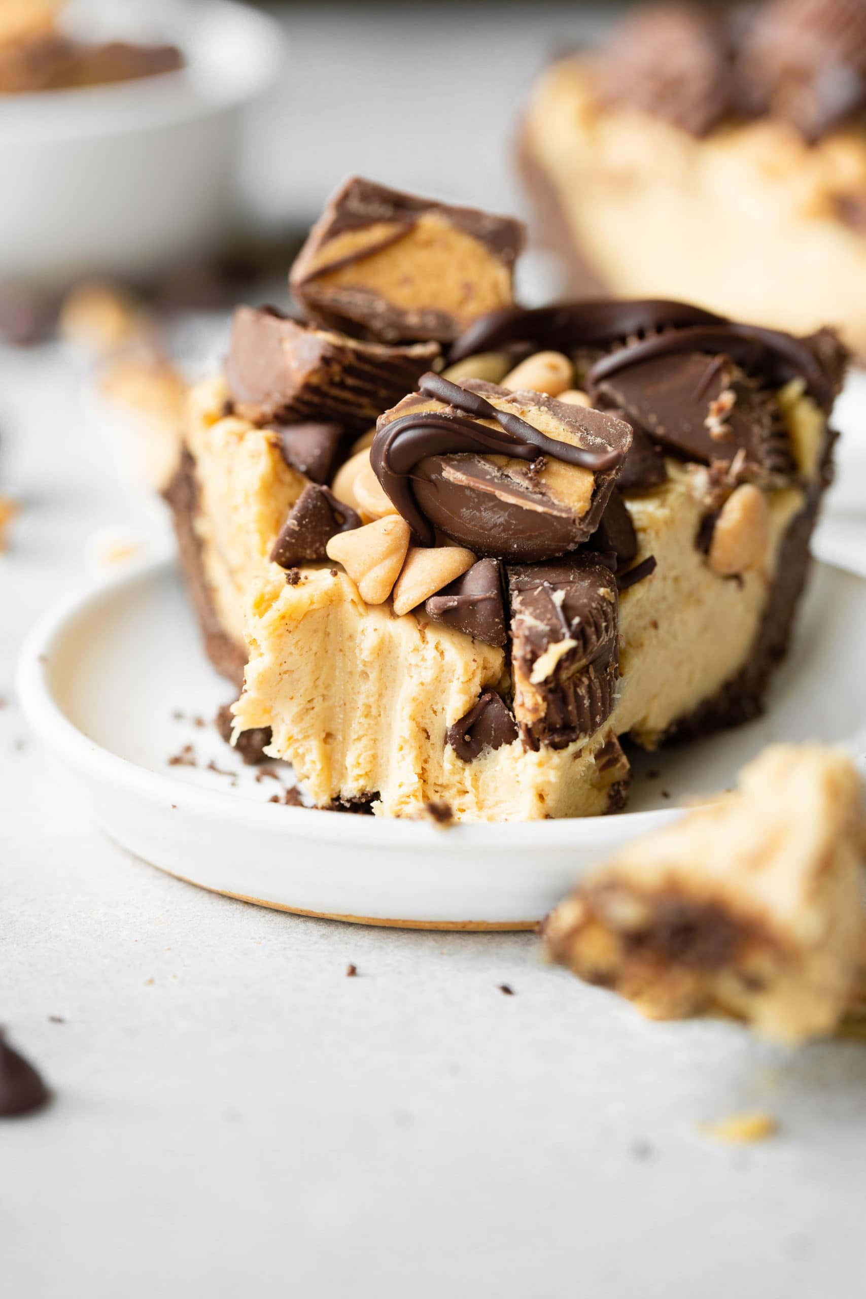 a photo of a piece of peanut butter pie with bite taken out it topped with peanut butter cups and peanut butter and chocolate chips. a photo of a piece of peanut butter pie with bite taken out it topped with peanut butter cups and peanut butter and chocolate chips.