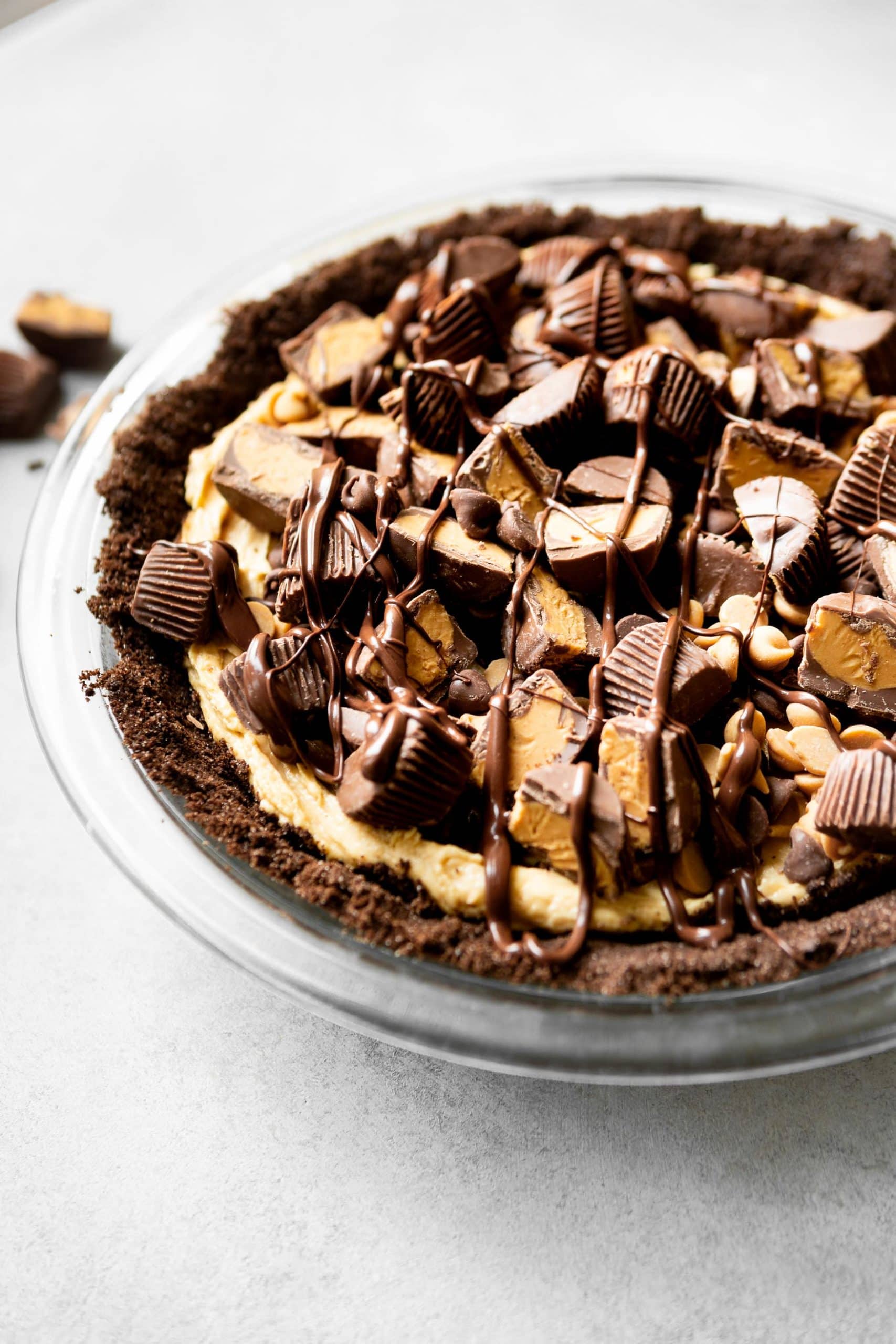 a photo of a peanut butter pie with a chocolate graham cracker crust topped with mini peanut butter cupes, chocolate chips and peanut butter chips with a chocolate drizzle. a photo of a peanut butter pie with a chocolate graham cracker crust topped with mini peanut butter cupes, chocolate chips and peanut butter chips with a chocolate drizzle.