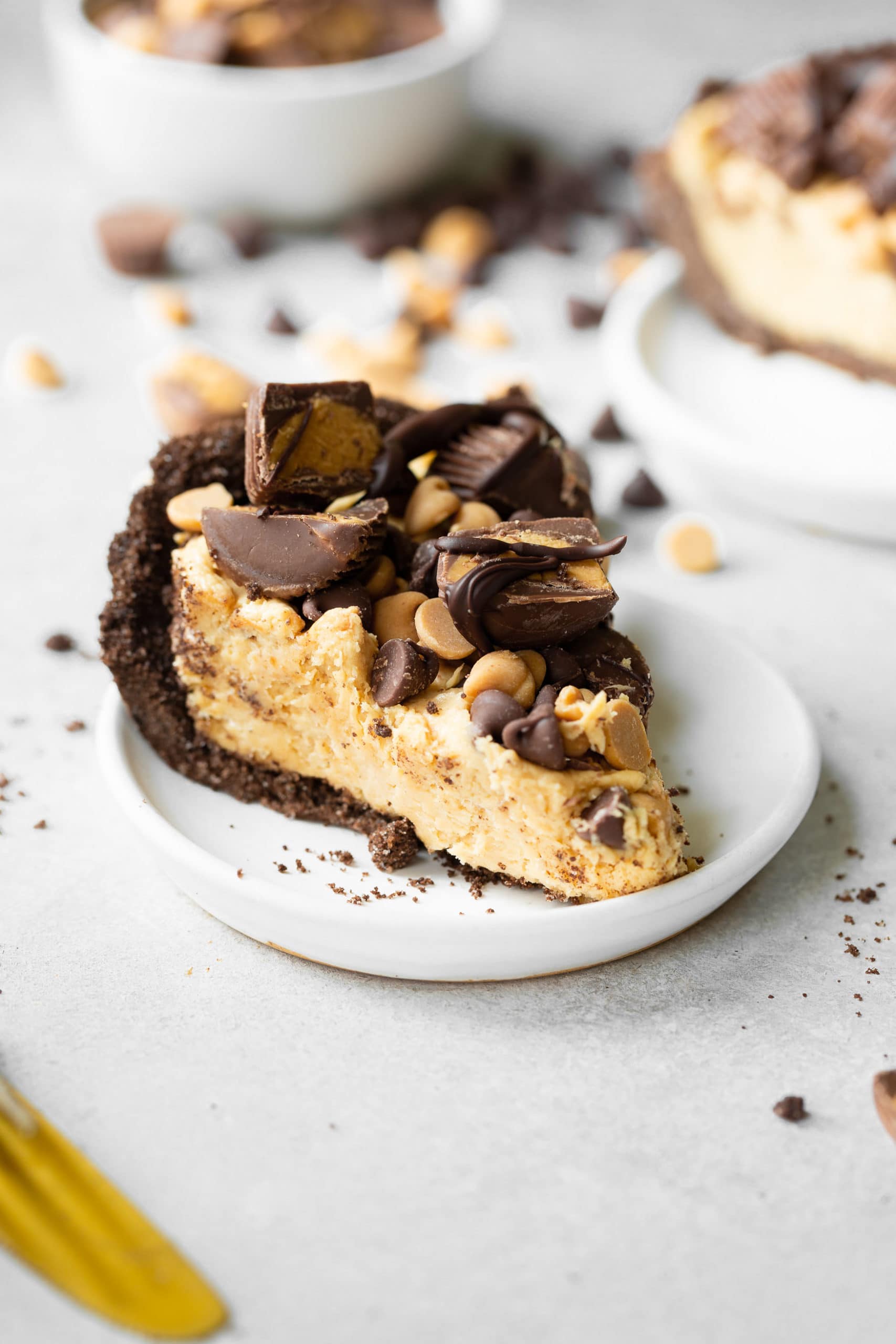 a photo of a slice of peanut butter pie on a small white saucer. the pie is topped with peanut butter cups and chocolate chips and peanut butter chips. a photo of a slice of peanut butter pie on a small white saucer. the pie is topped with peanut butter cups and chocolate chips and peanut butter chips.