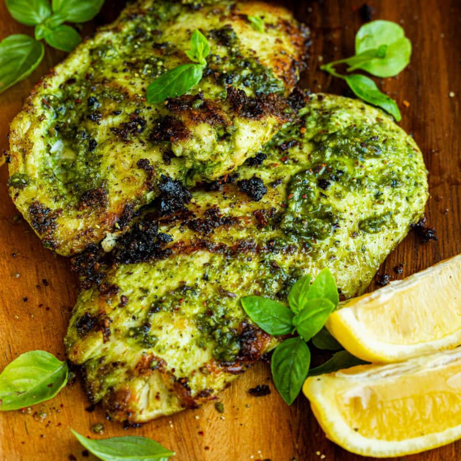 a photo taken over the top of two grilled chicken breasts coated in basil sitting on a cutting board with lemon wedges sitting next to them a photo taken over the top of two grilled chicken breasts coated in basil sitting on a cutting board with lemon wedges sitting next to them