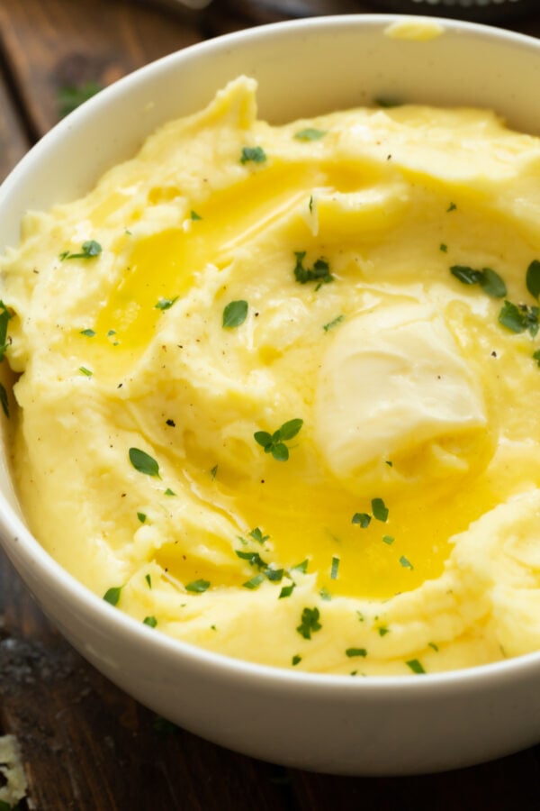 a photo of a large serving bowl full of creamy mashed potatoes topped with a pat of melting butter and sprinkled with parsley. a photo of a large serving bowl full of creamy mashed potatoes topped with a pat of melting butter and sprinkled with parsley.